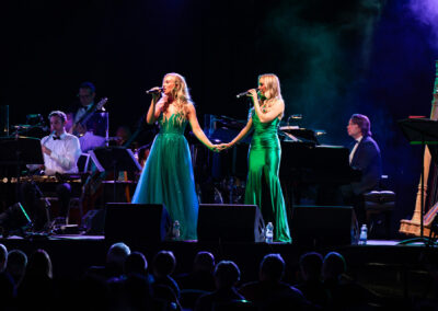 Shona and Leah hold hands and sing on stage